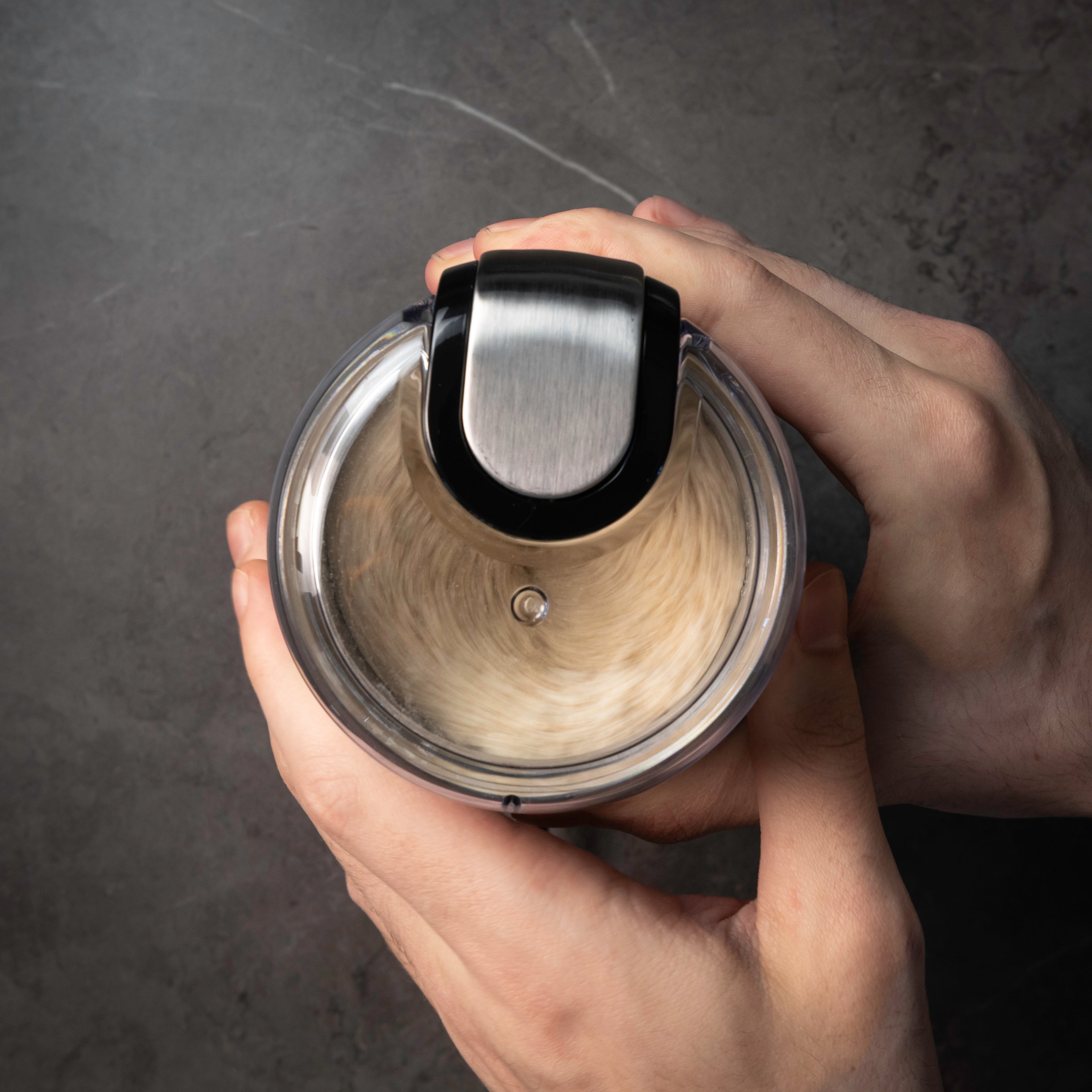 Hand holding a coffee grinder with milled wheat inside, against a dark background