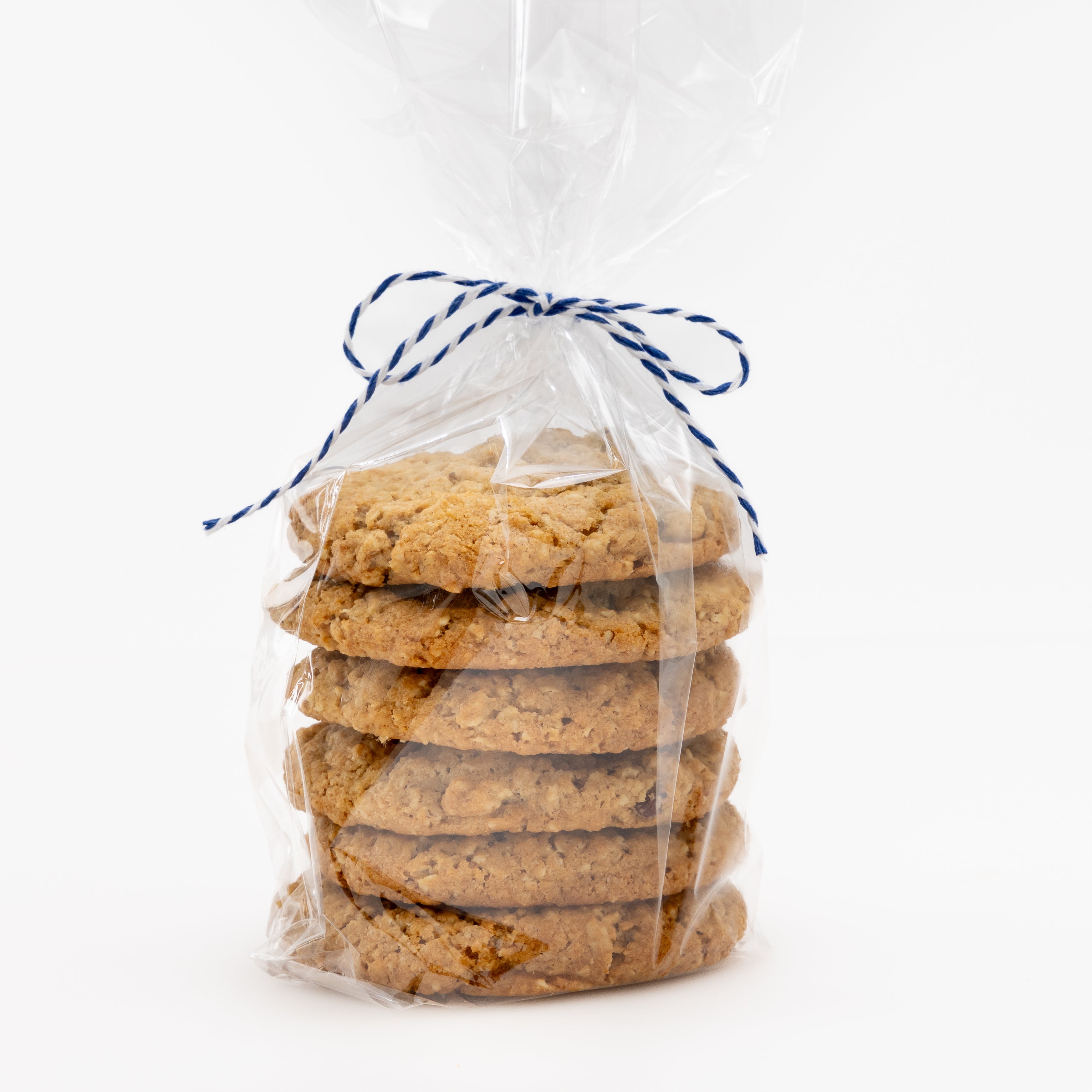 A stack of six golden-brown cookies sealed in a clear cellophane bag and tied with a blue-and-white striped string, photographed on a white background.