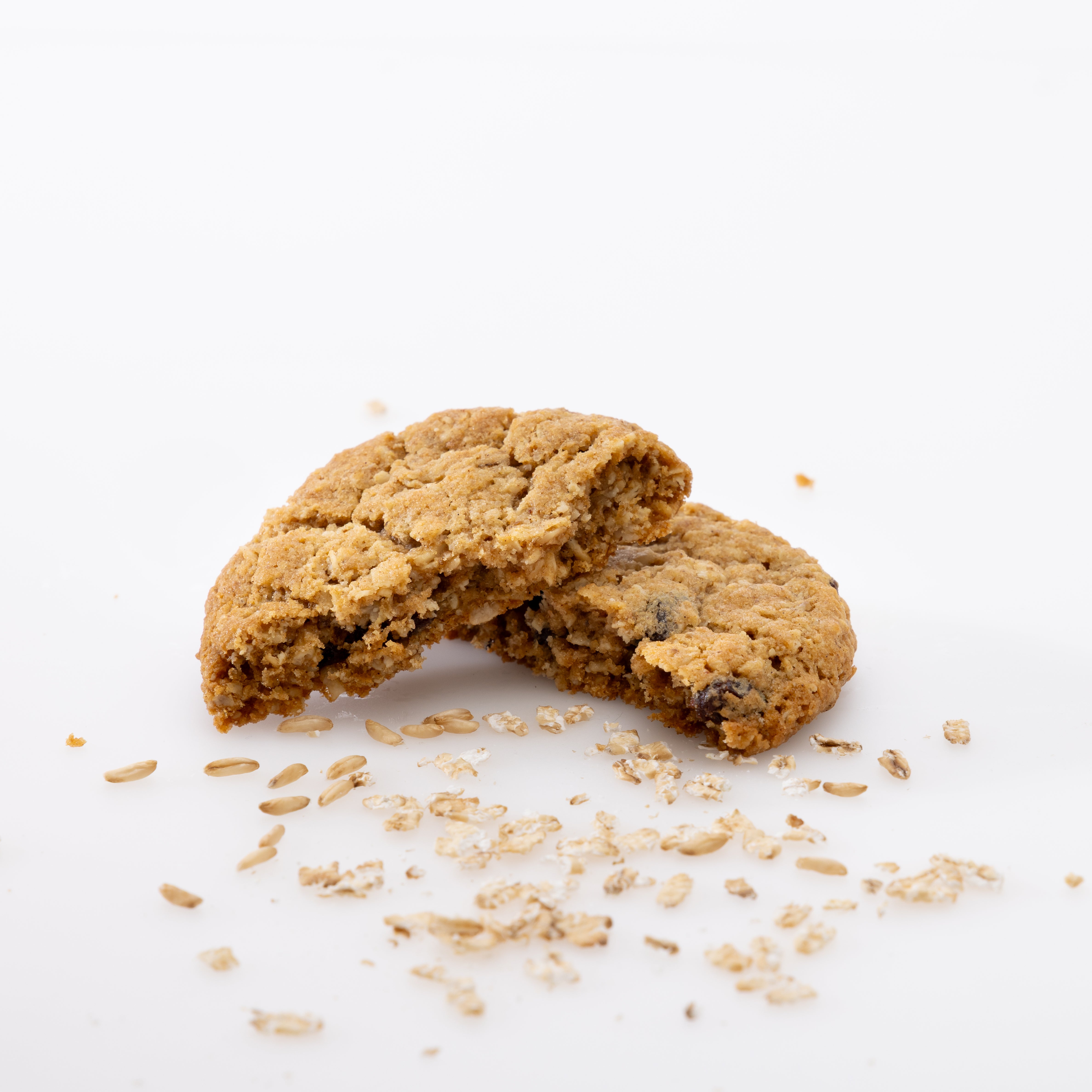 A broken oatmeal cookie with visible chunks and scattered oats on a clean white background.