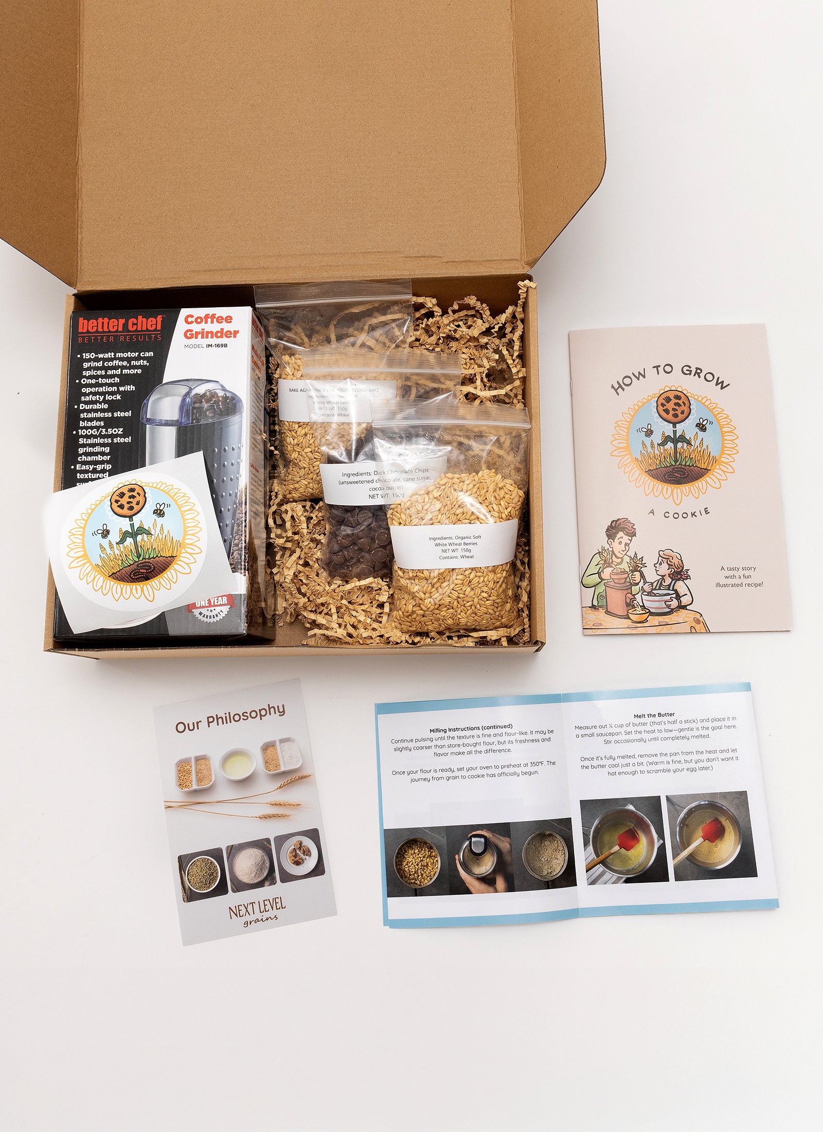 DIY cookie kit with coffee grinder included in box, chocolate chips, grains and a children's storybook on a white background